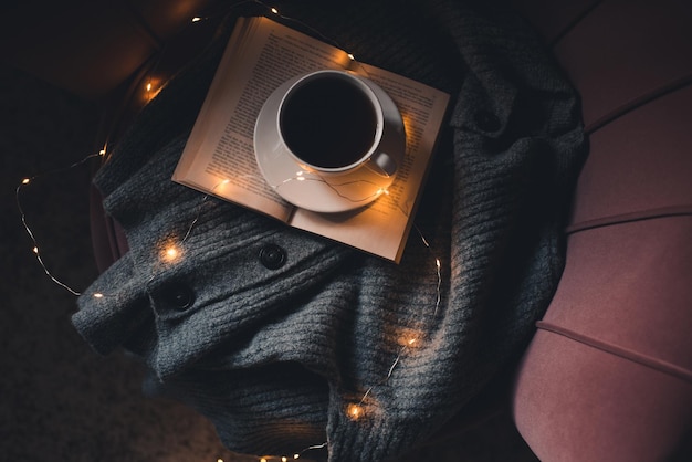 Xícara de café fica na bok de papel aberta com camisola de malha no sofá close-up. Trabalhar em casa à noite.