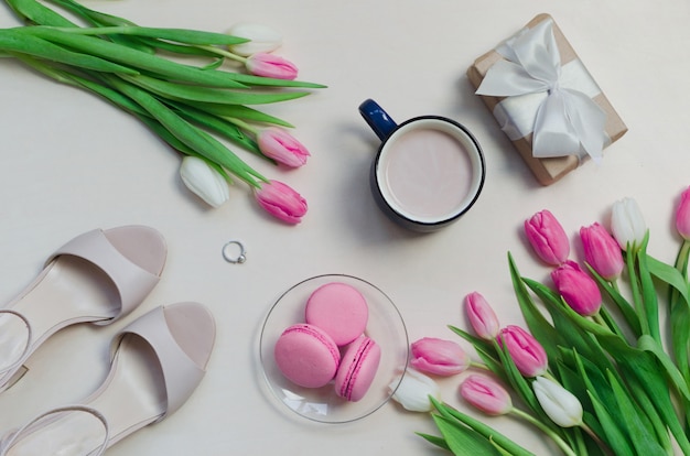 Xícara de café, flores de tulipa primavera e macarons rosa na vista superior de mesa pastel.