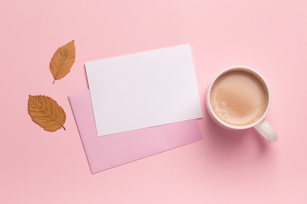 Xícara de café, folhas de outono e papel pf em branco sobre fundo rosa pastel, espaço de cópia