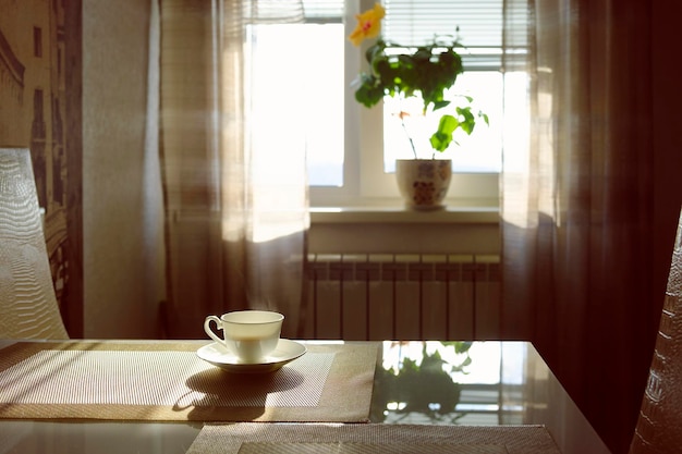 Xícara de café fumegante quente em uma manhã ensolarada na mesa da cozinha