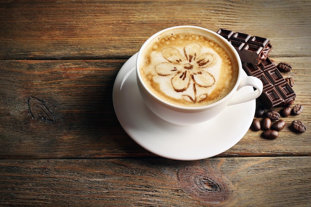 Xícara de café latte art com grãos e chocolate em fundo de madeira