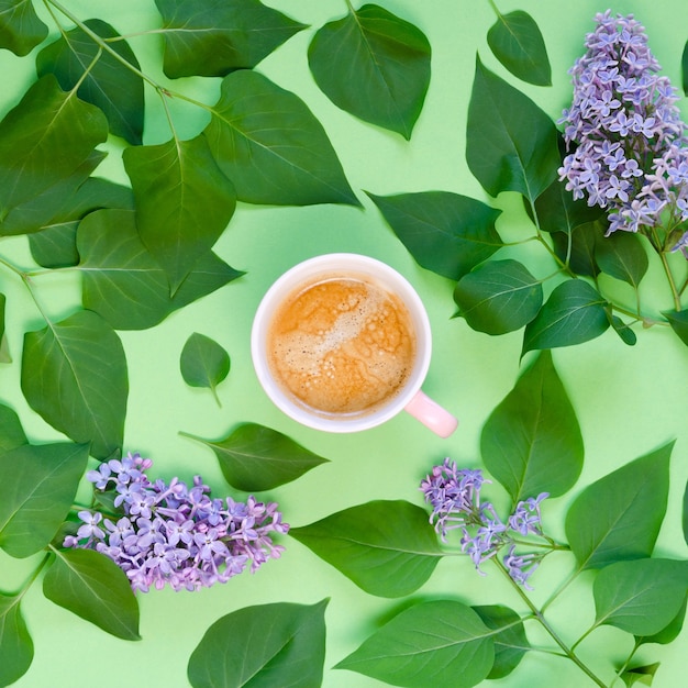 Xícara de café, lilás e folhas verdes em uma mesa verde. Vista do topo