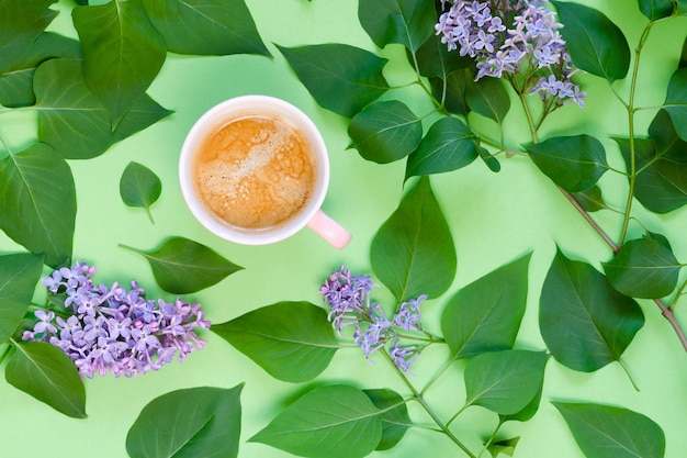 Xícara de café, lilás e folhas verdes sobre um fundo verde. vista do topo