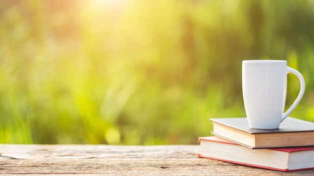 Xícara de café, livro e equipamento de jardim na mesa de madeira com luz solar no tempo da manhã