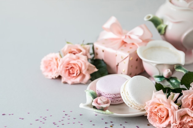 Xícara de café, macarrão para bolo, um presente em uma caixa e rosas cor de rosa em uma superfície cinza