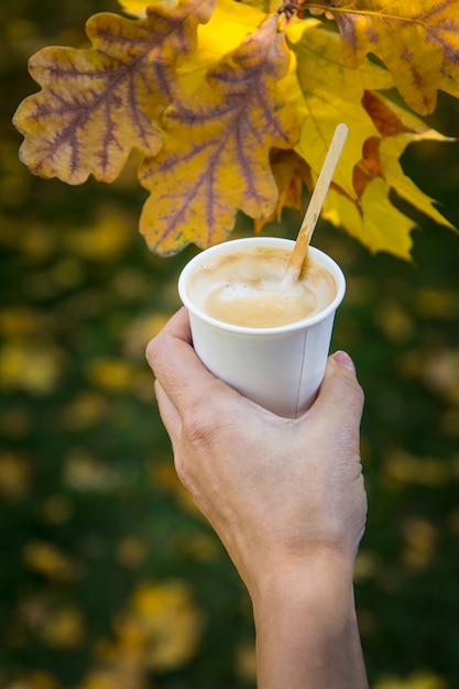 Xícara de café na mão de uma mulher com folhas de outono no fundo