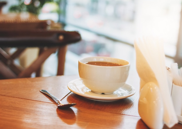 Xícara de café na mesa de madeira de café contra a janela na manhã
