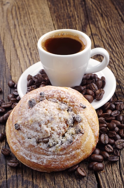 Xícara de café, pão doce e grãos de café na mesa de madeira