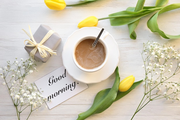 Xícara de café para flores de presente de café da manhã e cartão com palavras Bom dia na vista superior da mesa