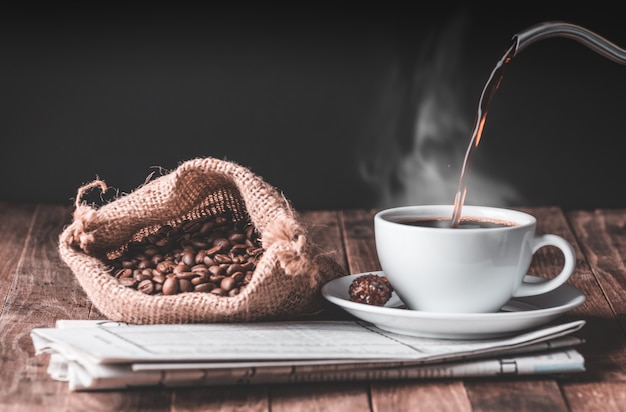 Xícara de café, pau de canela, grãos de café torrados e jornal na mesa de madeira