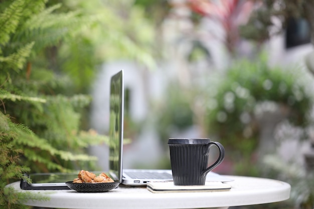 Xícara de café preta e vista lateral do laptop com tablet e biscoitos