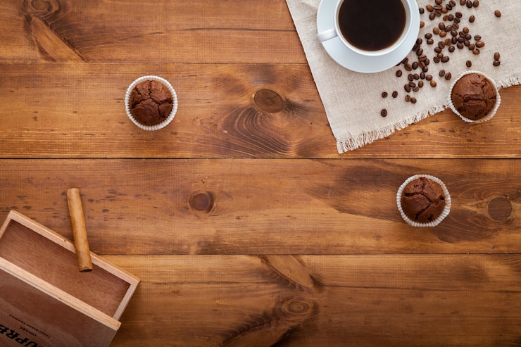 Foto xícara de café preto, bolos e grãos de café espalhados na mesa de madeira marrom