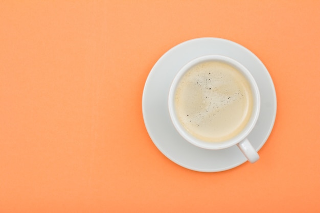 Xícara de café preto de porcelana branca em pires em fundo de cor de pêssego. Vista superior com espaço de cópia