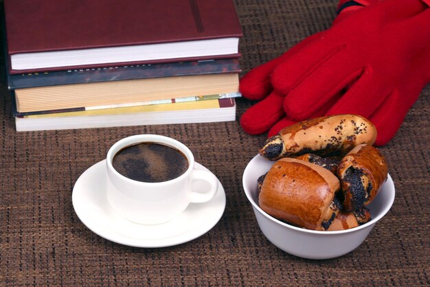 Xícara de café preto e pãezinhos com papoula perto dos livros e luvas vermelhas