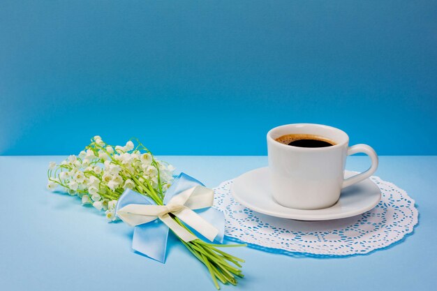 Xícara de café preto em um pires e um buquê de flores de lírio do vale