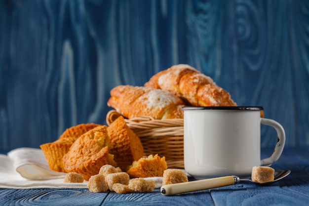 Xícara de café preto em uma caneca de esmalte velha, croissants de café da manhã no fundo, mesa rústica vintage