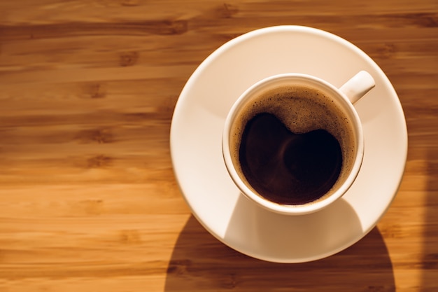 Xícara de café preto na mesa de bambu sob o sol da manhã