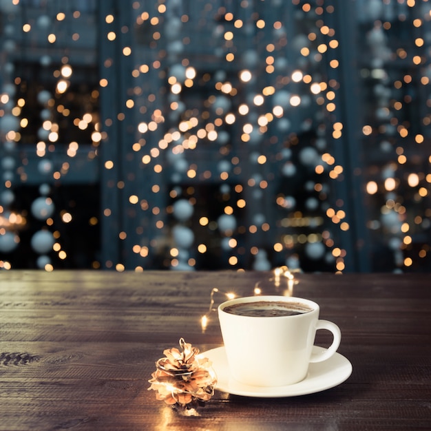 Xícara de café preto na mesa de madeira no café. luzes de natal e guirlanda de ouro sobre fundo.