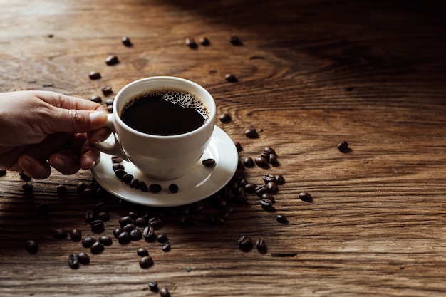 Xícara de café preto quente e grãos de café na mesa de madeira com luz natural pela manhã