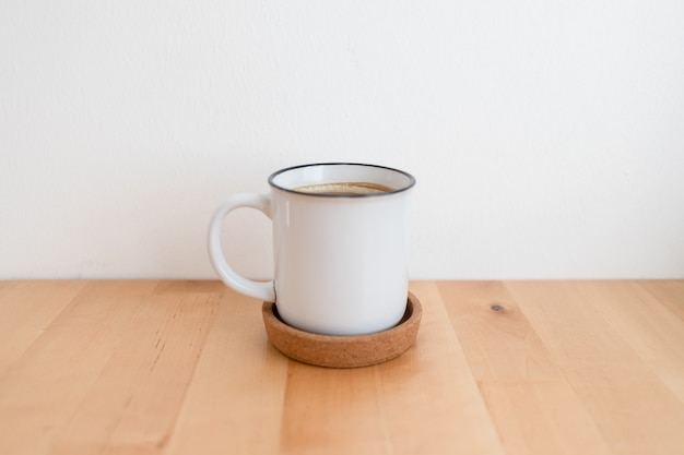 Xícara de café quente branca na mesa de madeira e parede branca com espaço de cópia.