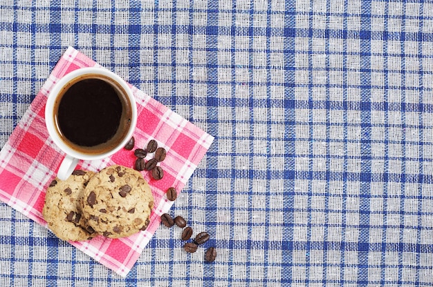 Xícara de café quente com biscoitos de chocolate em uma toalha de mesa azul, vista de cima