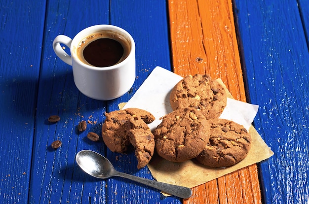 Xícara de café quente com biscoitos de chocolate na mesa de madeira colorida