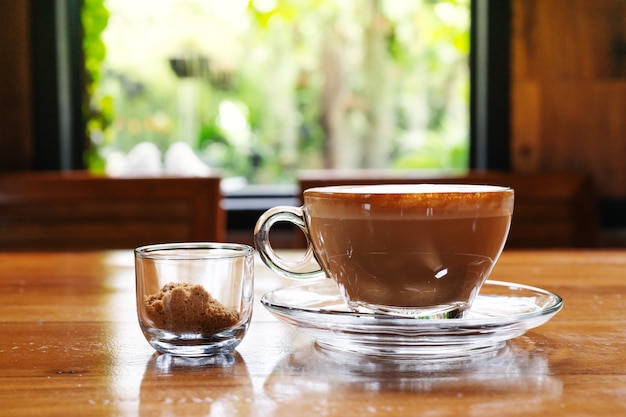 Xícara de café quente com cana-de-açúcar na mesa de madeira, vista da janela