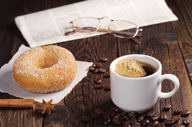 Xícara de café quente com donut e jornal na velha mesa de madeira