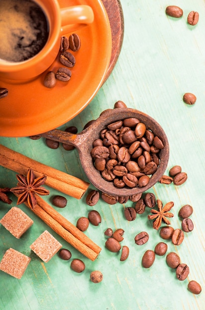 Xícara de café quente com espuma de leite, canela, anis estrelado e grãos de café na mesa de madeira