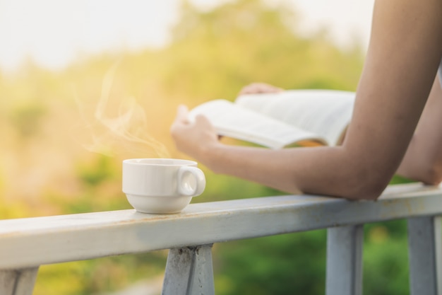 Foto xícara de café quente com mulher lendo livro ao ar livre