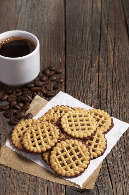 Xícara de café quente e biscoitos redondos com chocolate na velha mesa de madeira