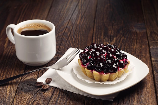 Xícara de café quente e bolo com groselha preta na mesa de madeira escura