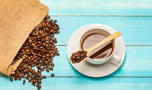 Xícara de café quente e grãos de café torrados do saco saco em uma mesa de madeira e colher.