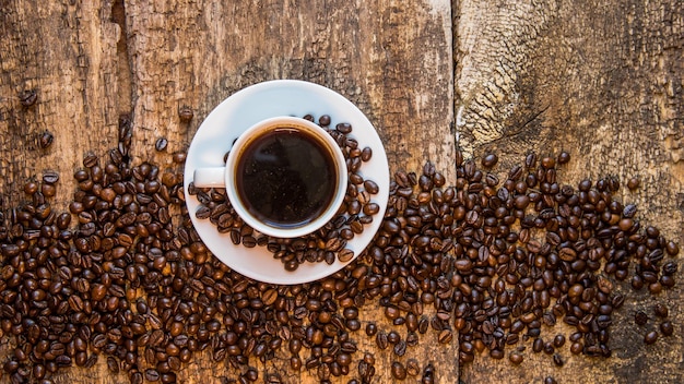 Xícara de café quente e grãos de café torrados em uma mesa de madeira Fundo escuro