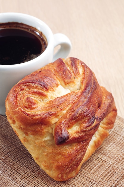 Xícara de café quente e pão doce na mesa de madeira