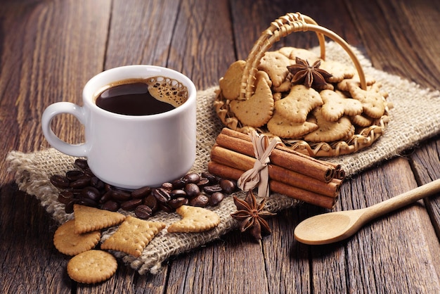Xícara de café quente e pequenos biscoitos decorativos em uma cesta de vime na velha mesa de madeira