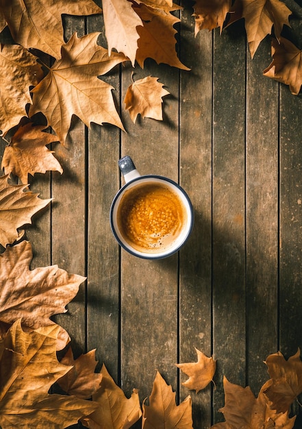 Xícara de café quente em uma mesa de madeira envelhecida com folhas de outono ao redor. Sentimento caseiro e relaxamento