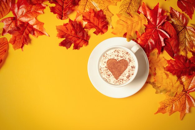 Xícara de café romântica com folhas de outono em fundo amarelo. Vista do topo