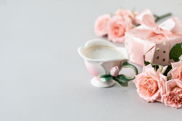 Foto xícara de café, rosas cor de rosa, caixa com um presente e rosas cor de rosa em uma superfície cinza