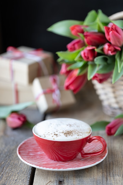 Xícara de café vermelho close-up, um buquê de tulipa vermelha e caixas de presente com fundo de madeira