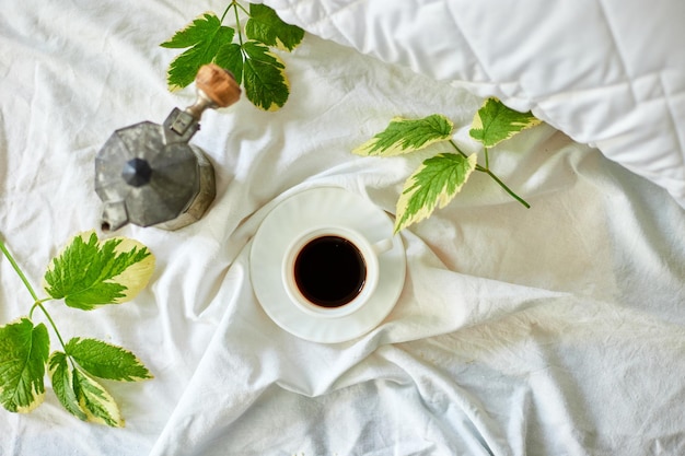 Xícara de café vista superior em lençóis brancos com cafeteira gêiser e folhas verdes