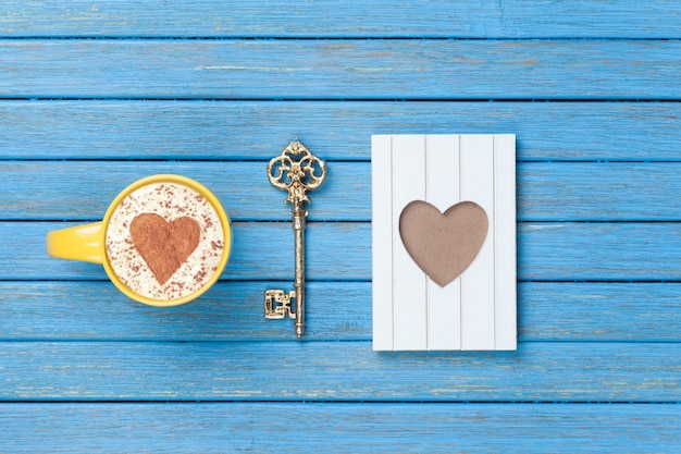 Xícara de Cappuccino com símbolo de forma de coração, chave e moldura de madeira azul.