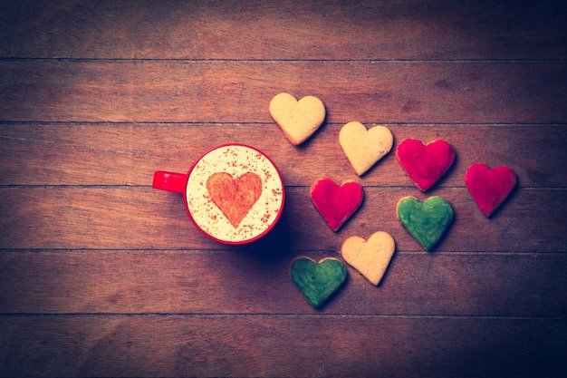 Xícara de Cappuccino com símbolo de forma de coração e biscoitos na madeira