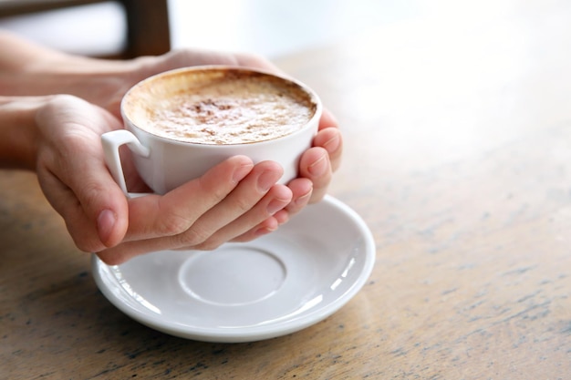 Xícara de cappuccino saboroso com as mãos na mesa