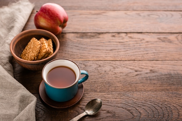 Xícara de chá, biscoitos e maçã em um fundo de madeira