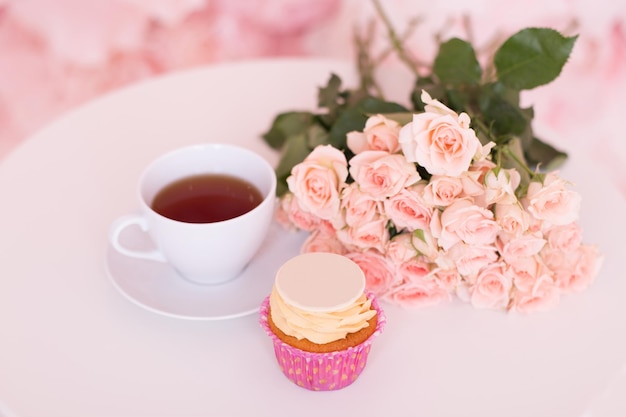 Xícara de chá, bolo doce e rosas cor de rosa no fundo da mesa branca