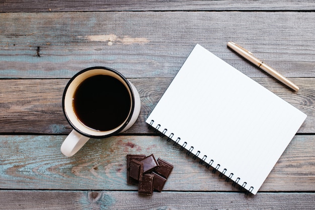 Xícara de chá, chocolate e uma caneta, caderno em uma mesa de madeira, flatlay