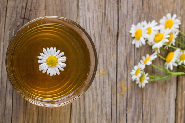 Xícara de chá com flores de camomila na mesa de madeira rústica.