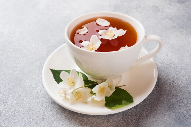 Xícara de chá com flores de jasmim em uma mesa cinza com espaço de cópia.