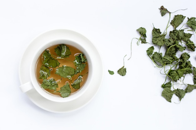 Xícara de chá com folhas secas de gotu kola em fundo branco